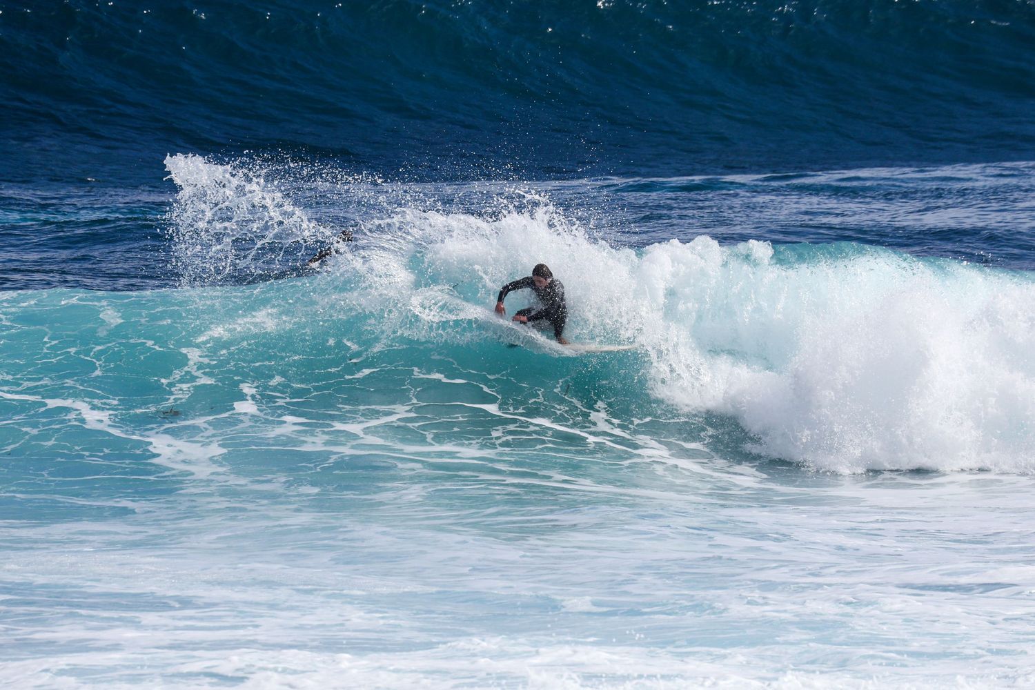 Surfer carving through a powerful blue ocean wave with white spray.