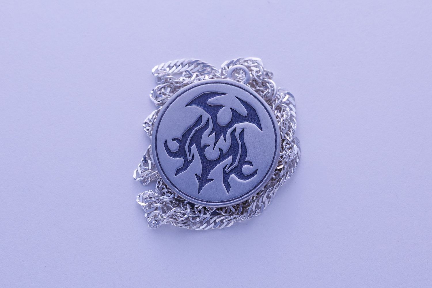 Round silver pendant necklace featuring engraved tribal flame design on decorative chain.