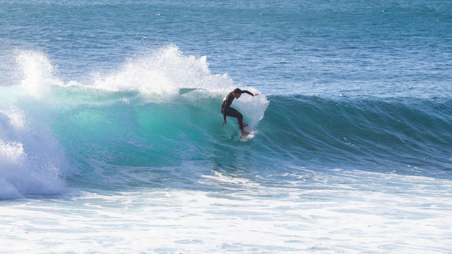 Surfer performing a sharp turn on a bright turquoise breaking wave in the ocean.