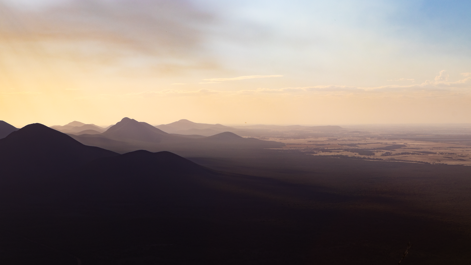 Aerial panoramic view of layered mountain ranges at golden sunset with hazy sky.
