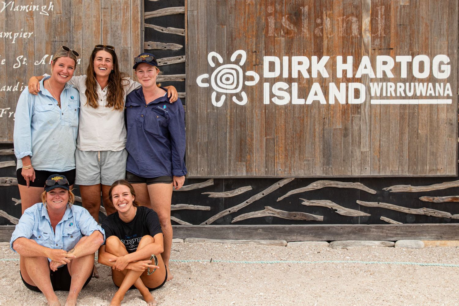 Five smiling visitors posing in front of the Dirk Hartog Island Wirruwana wooden sign in Western Australia.