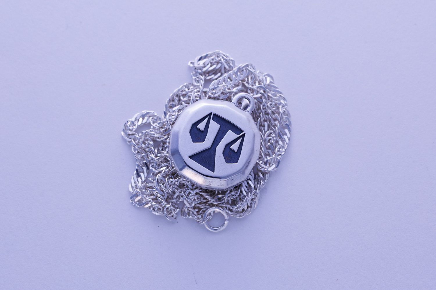 Round silver pendant necklace with engraved scales of justice symbol on rope chain.