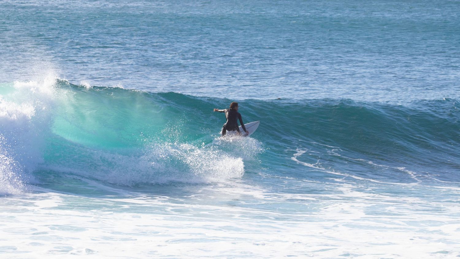 Surfer in a wetsuit riding a turquoise breaking wave.