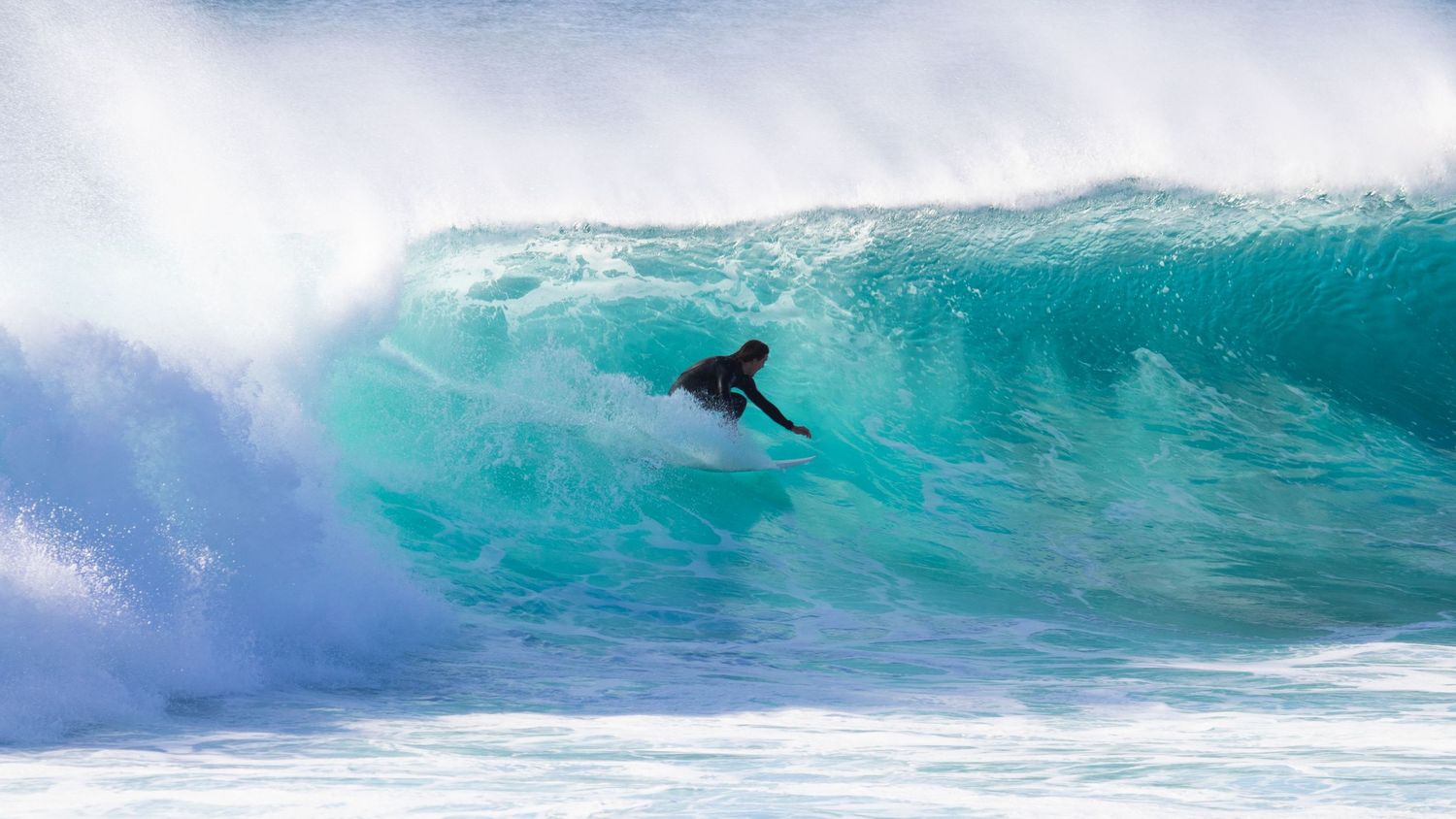 Surfer in black wetsuit riding inside a massive turquoise barrel wave.