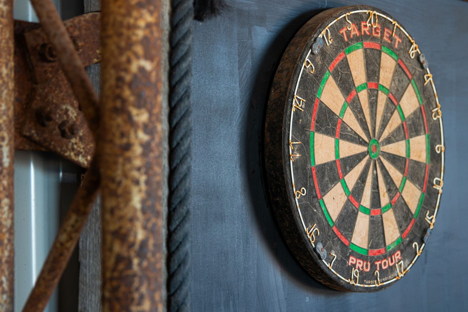 Vintage dartboard mounted on weathered blue wall beside rusty metal chains in rustic outback setting.