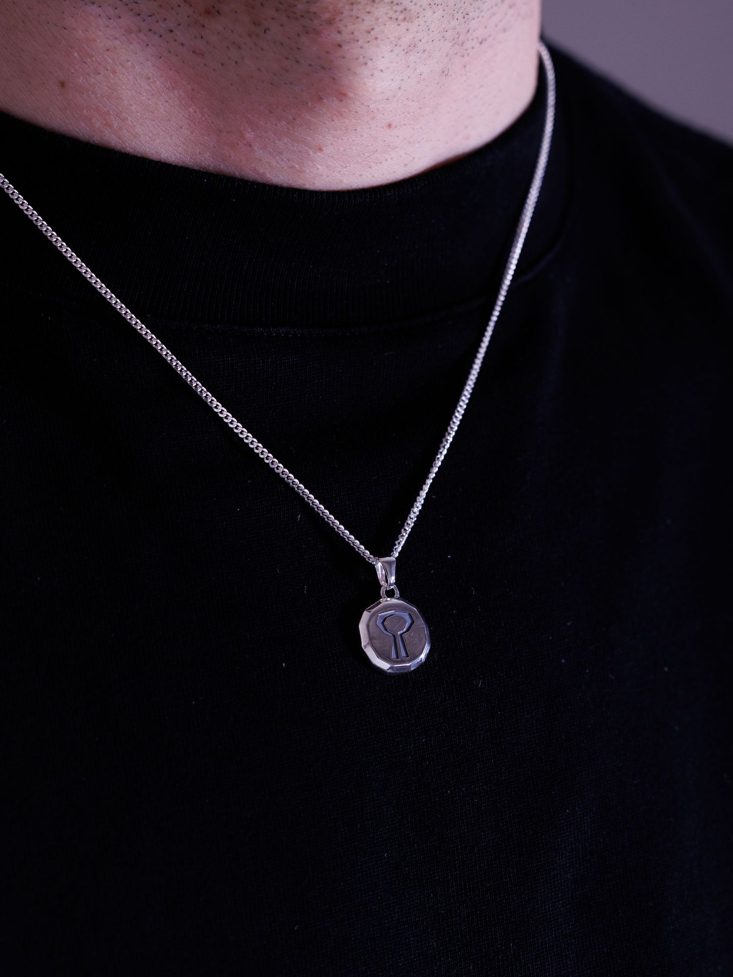 Man wearing silver keyhole engraved round pendant on curb chain necklace.