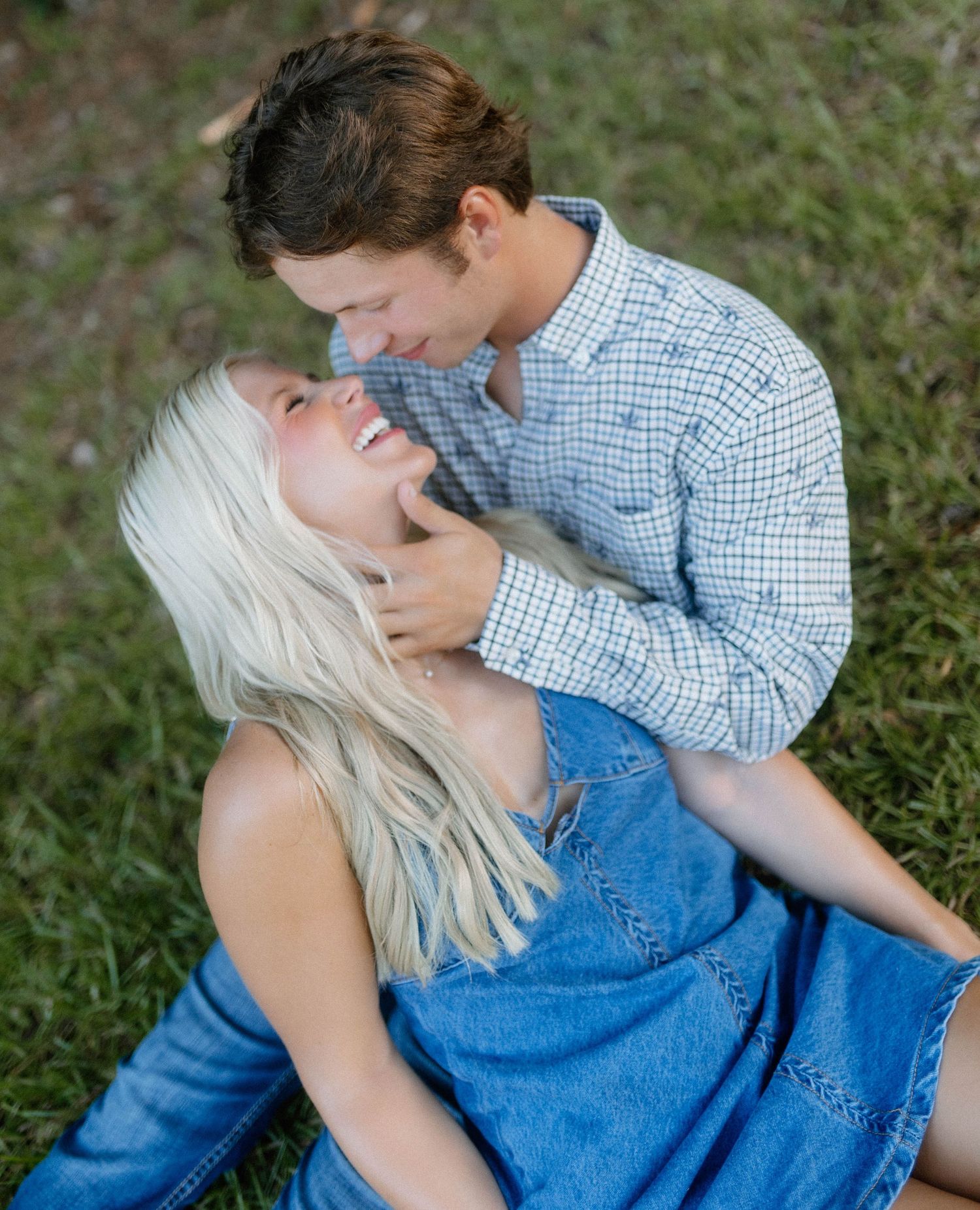 A couple in casual attire share an intimate moment while sitting together on grass outdoors.