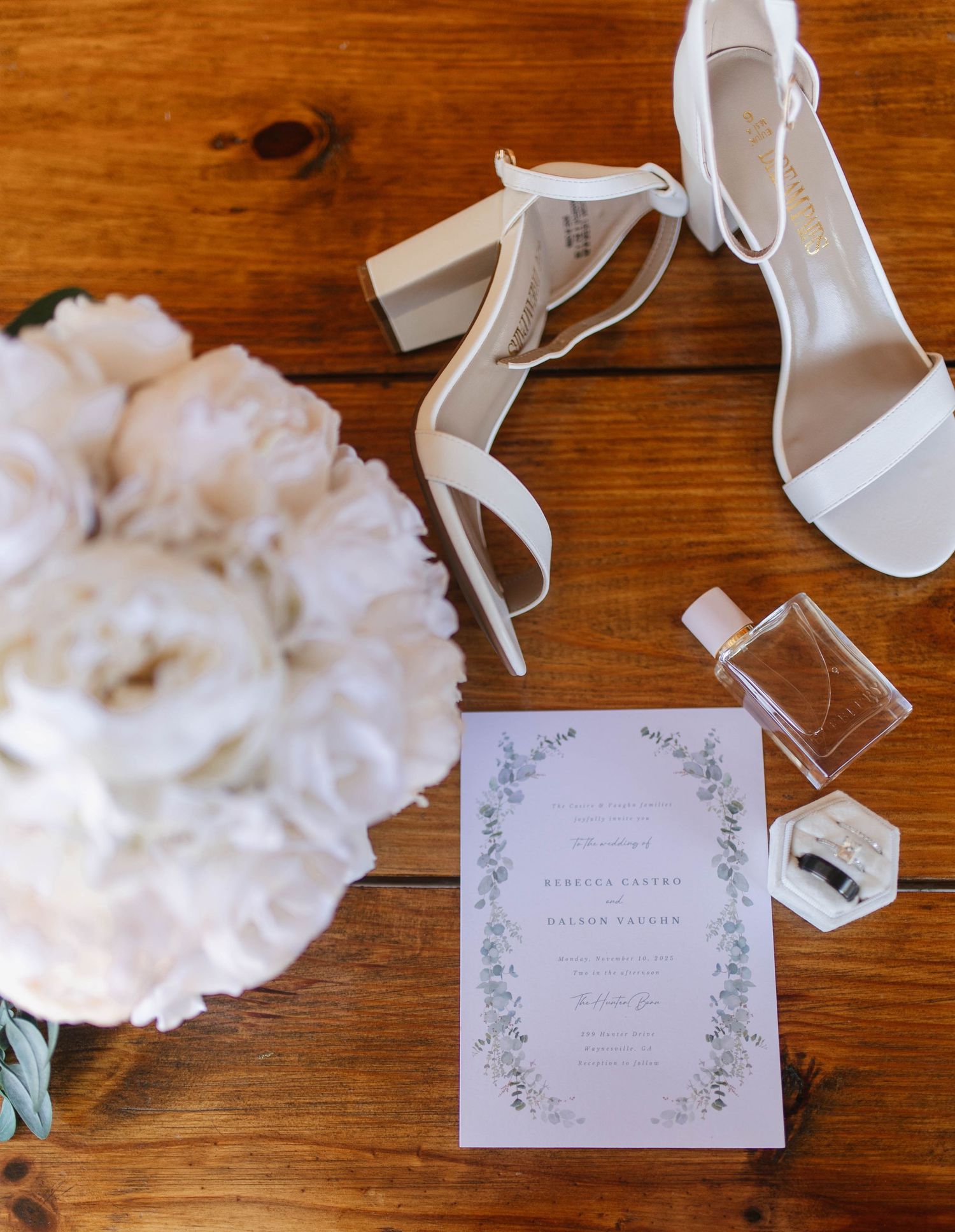 Wedding invitation and white decorative elements including ribbons and cotton arranged on a wooden surface.