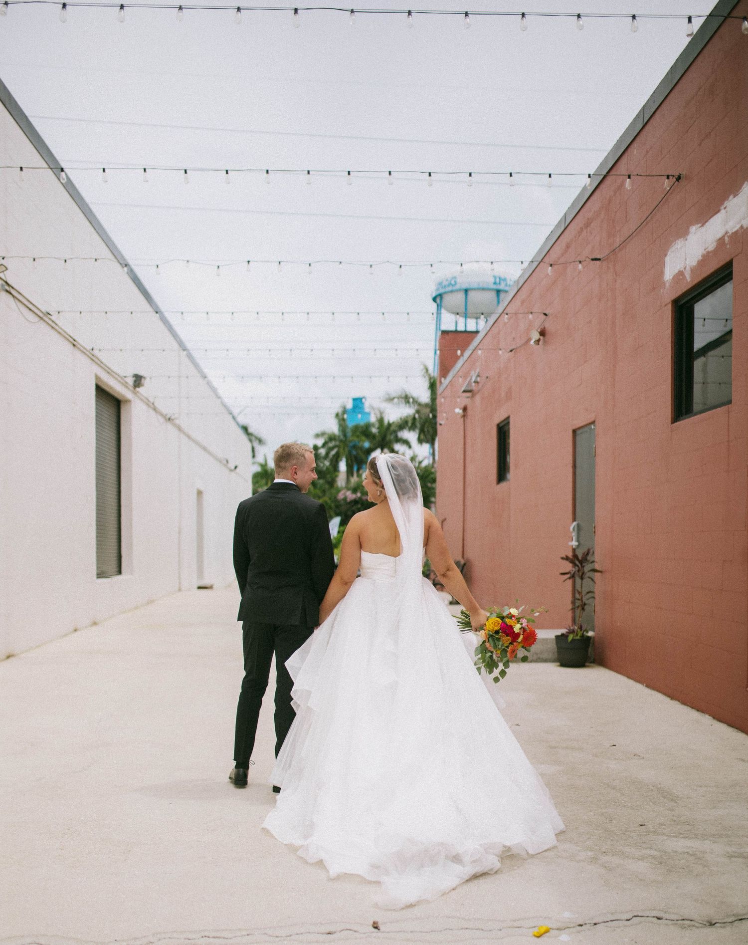 A wedding couple walks down a rustic alleyway with white walls and a terracotta colored building in sequence of shots.