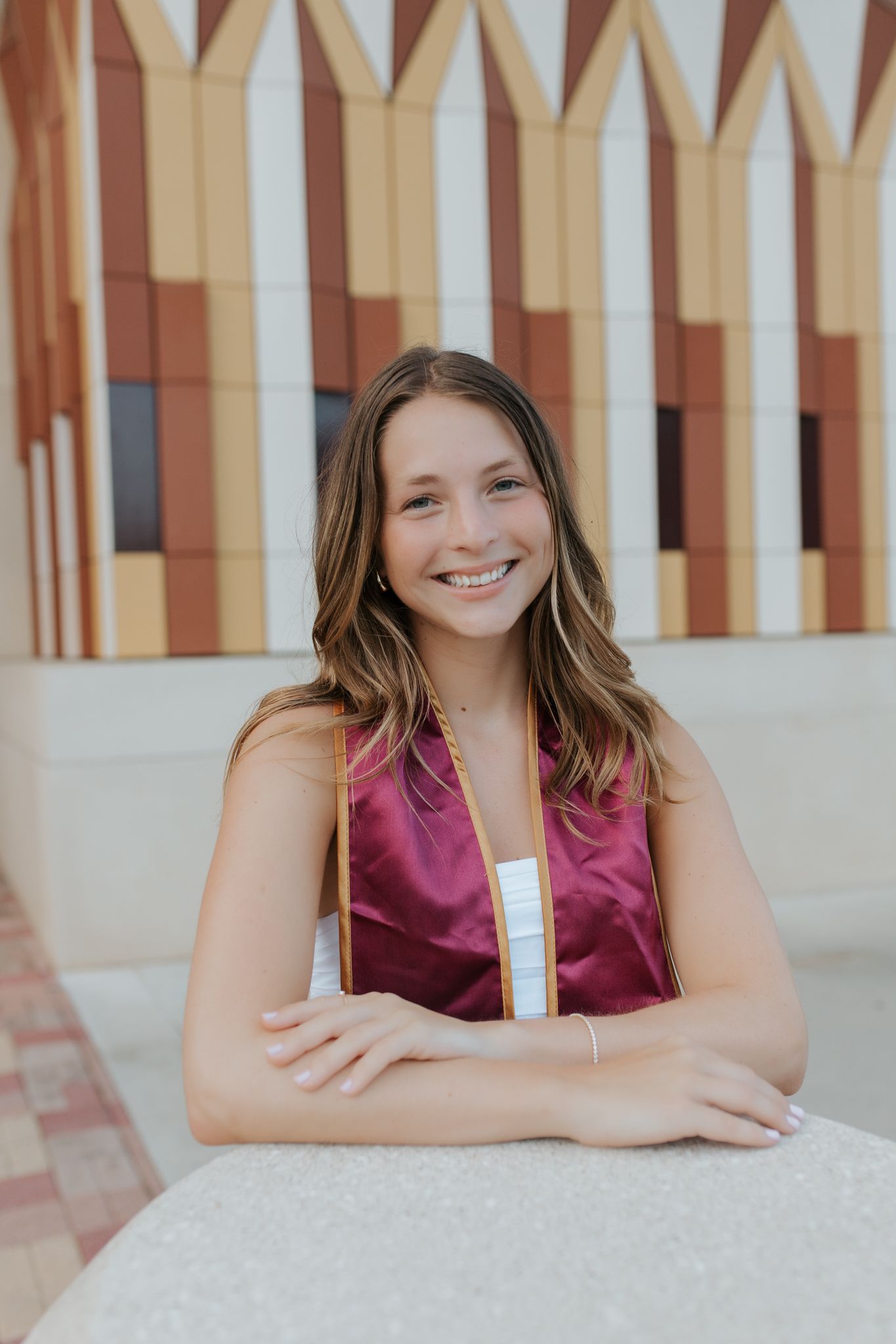 Professional headshot series against a neutral striped wall background showing relaxed poses and burgundy attire.