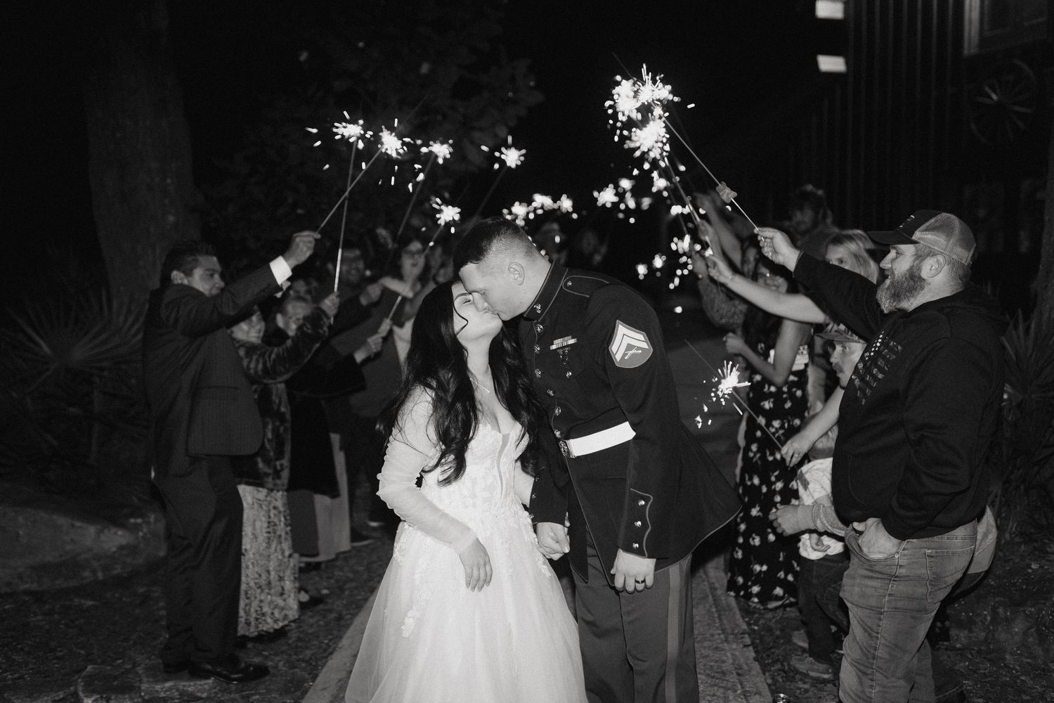 A group of people dance and celebrate at a lively wedding reception party on a dark dance floor.