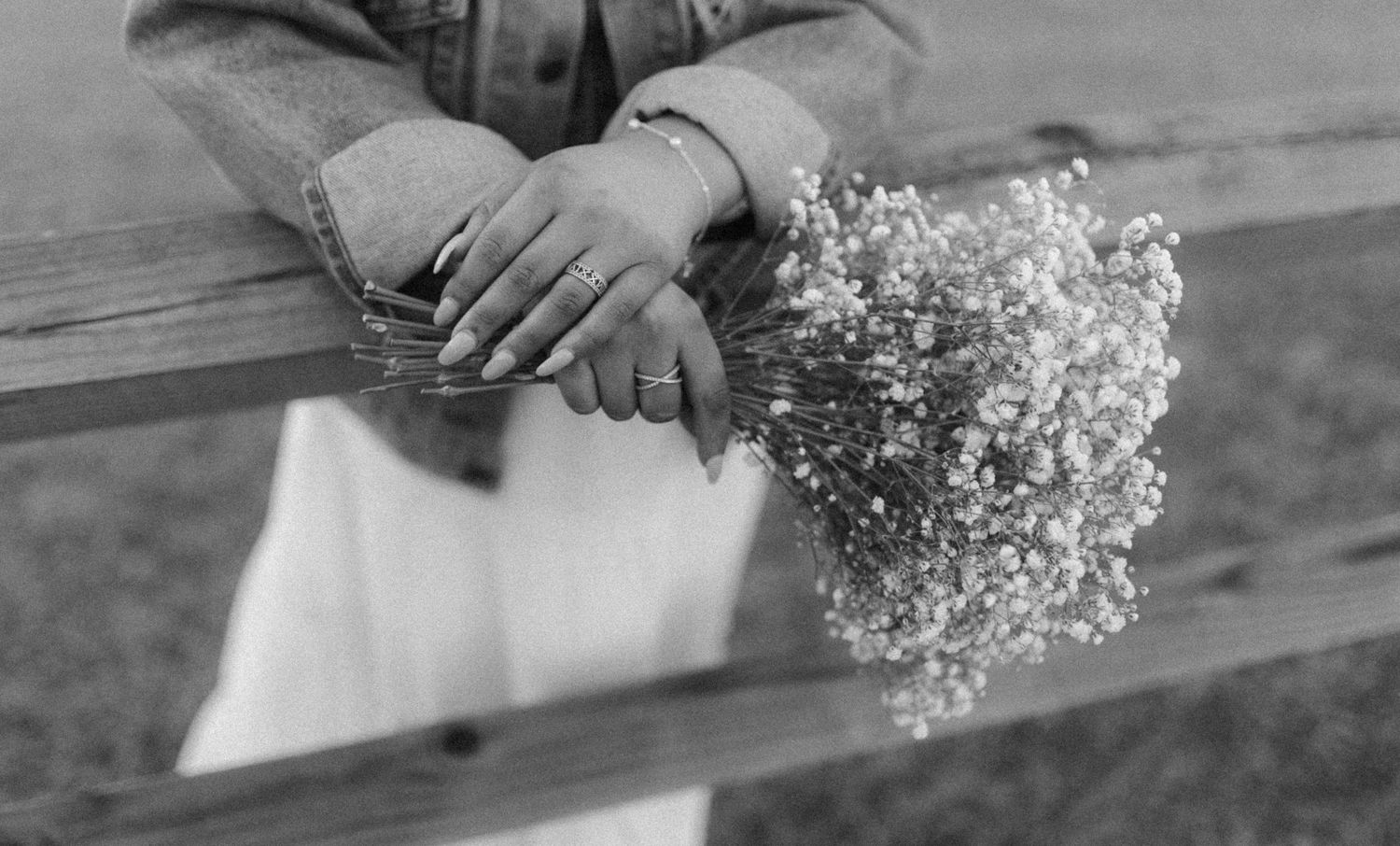 A black and white photograph shows hands holding a delicate bouquet of baby's breath flowers on a wooden surface.