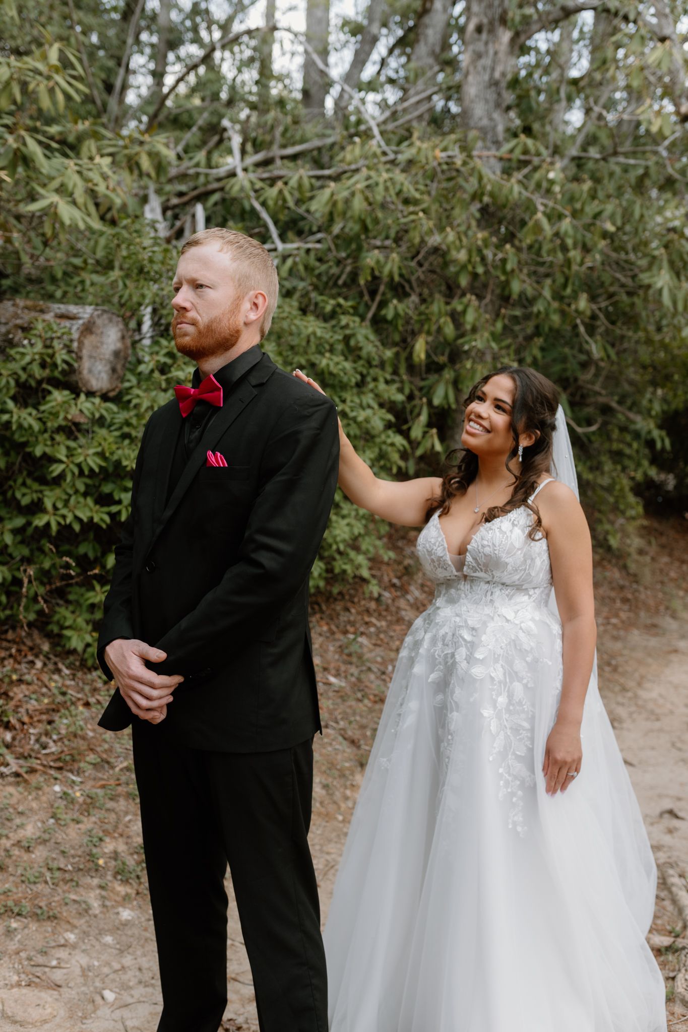 A couple shares joyful moments during their wedding photoshoot in a natural outdoor setting with lush greenery.