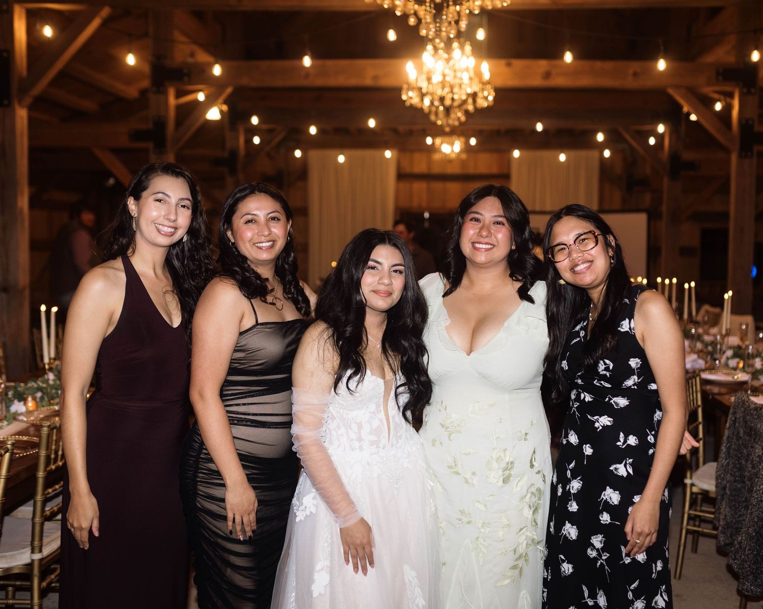 Wedding guests in black and white formal attire pose together under elegant crystal chandeliers at an evening reception.