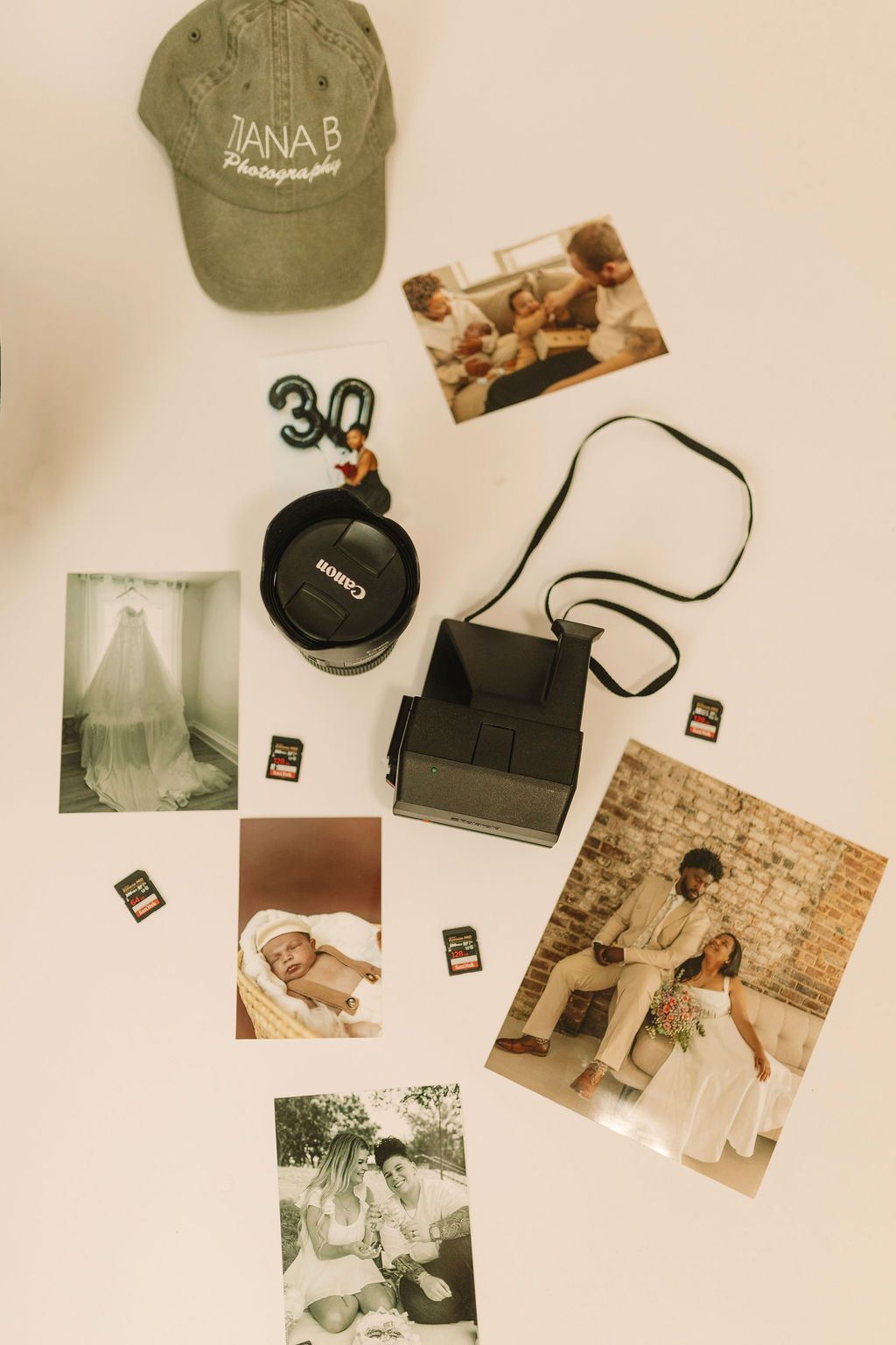 Flat lay of Canon camera, lens, SD cards, printed photos, a cap reading Dana B Photography, and a number 30 balloon charm.