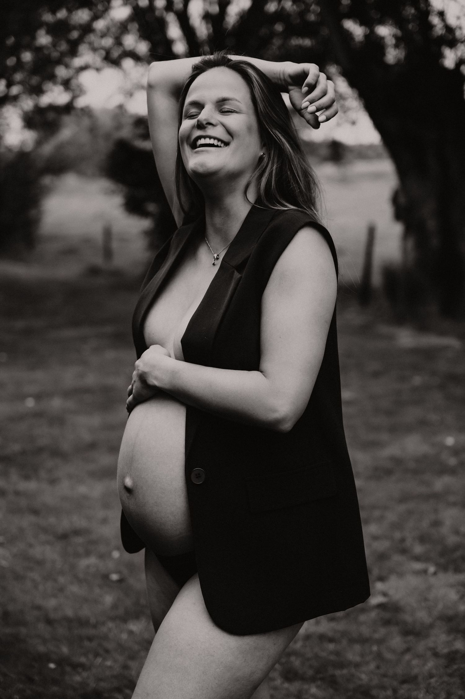 Zwangere vrouw poseert elegant in zwart-wit met donker vest buiten, zwangerschapsfotograaf West-Vlaanderen