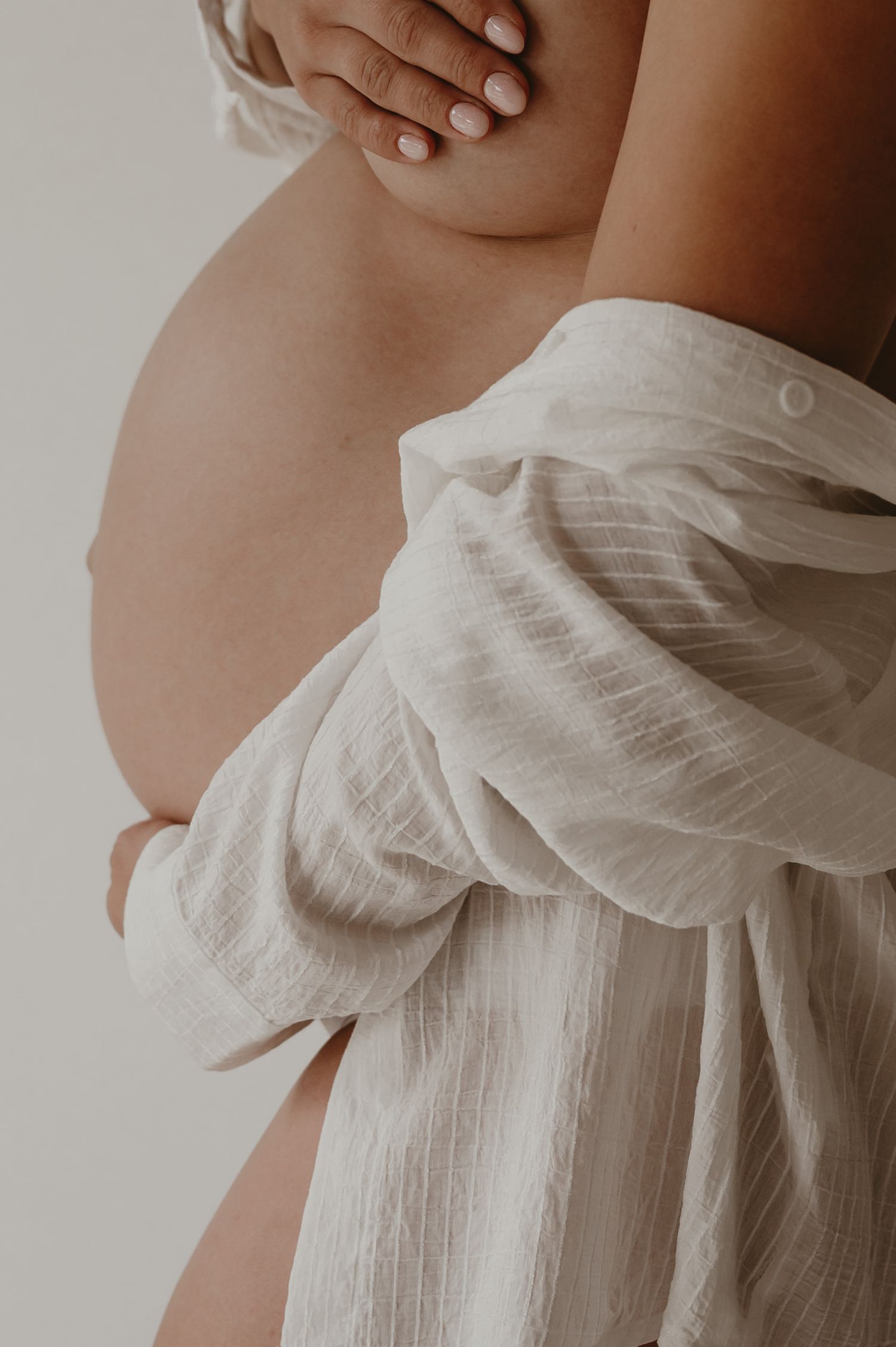 Zwangere vrouw omhuld in beige linnen doek, warme fine art zwangerschapsfotografie Roeselare