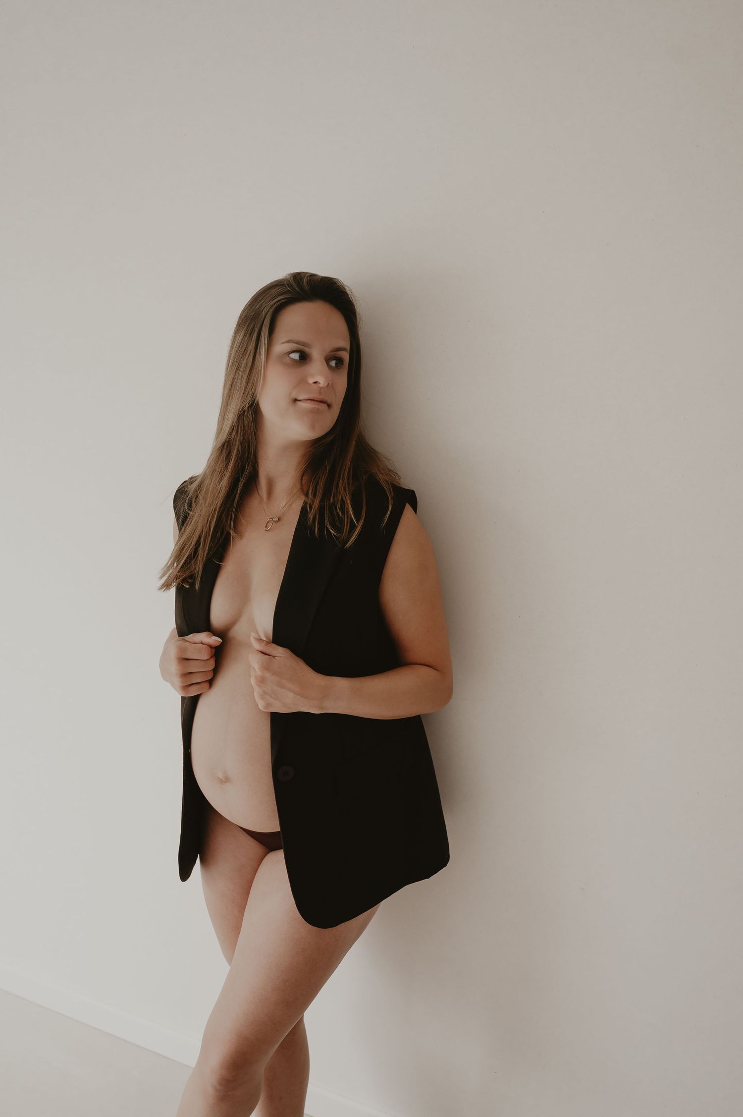 Zwangere vrouw in zwart mouwloos vestje poseert in studio, elegante zwangerschapsreportage fotograaf Roeselare