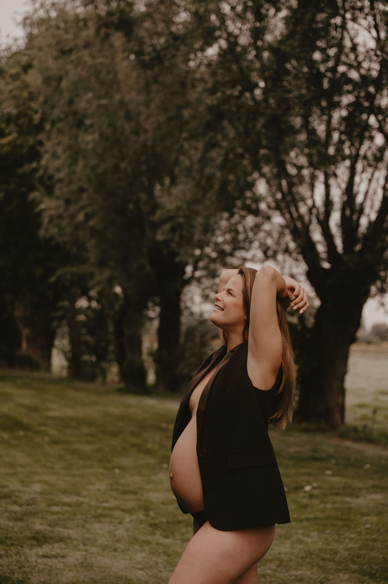 Zwangere vrouw staat in een park met warme herfstlichten, lifestyle zwangerschapsfotografie buiten Roeselare
