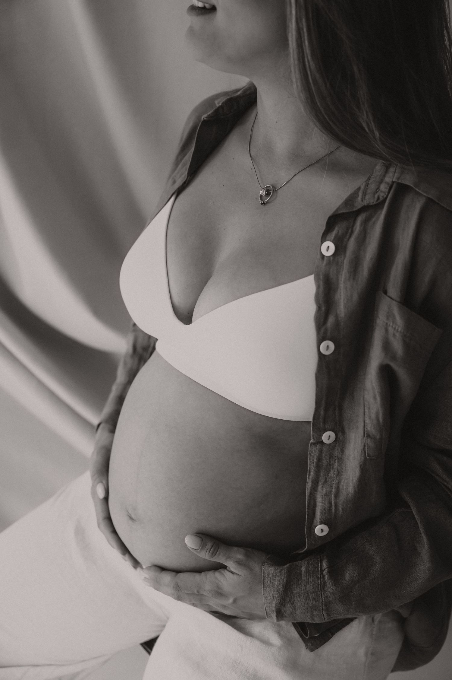 Zwangere vrouw in donker vest staat elegant met ronde buik, fine art zwangerschapsfotografie Roeselare