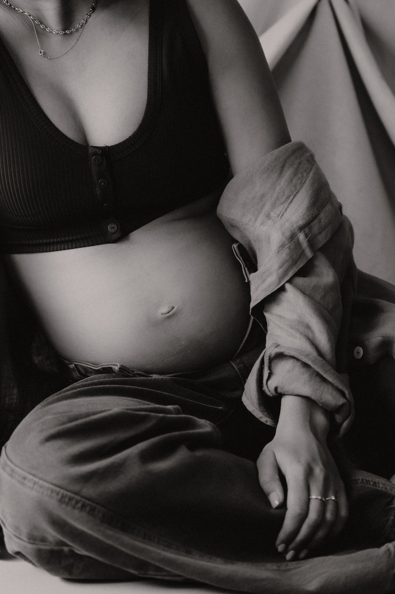 Zwangere vrouw zit neer met hand op buik in zwart-wit, intieme zwangerschapsfotografie zwangerschapsfotograaf Roeselare