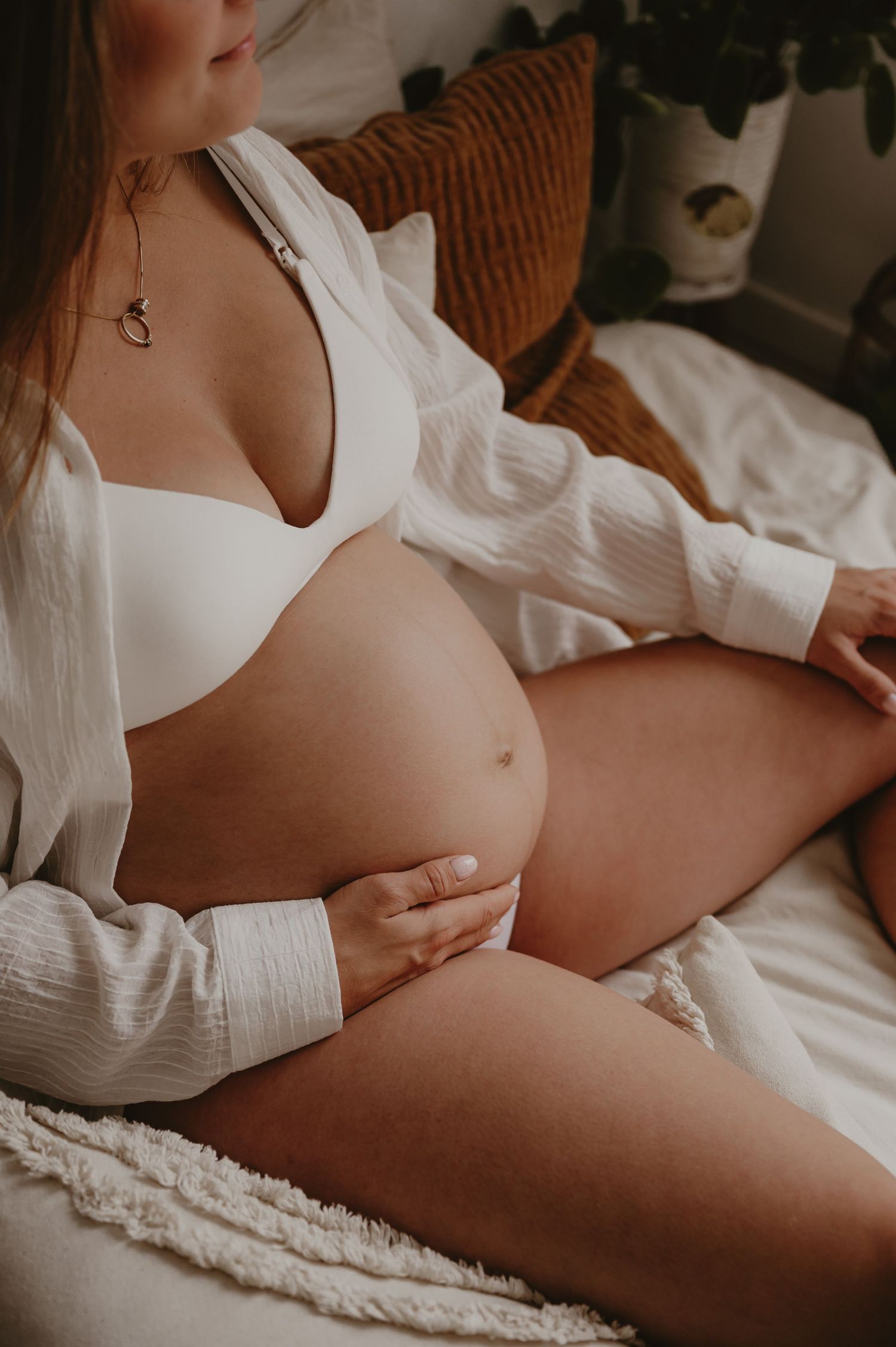 Zwangere vrouw in wit vest zit neer met stof om haar heen, lifestyle zwangerschapsfotografie Roeselare
