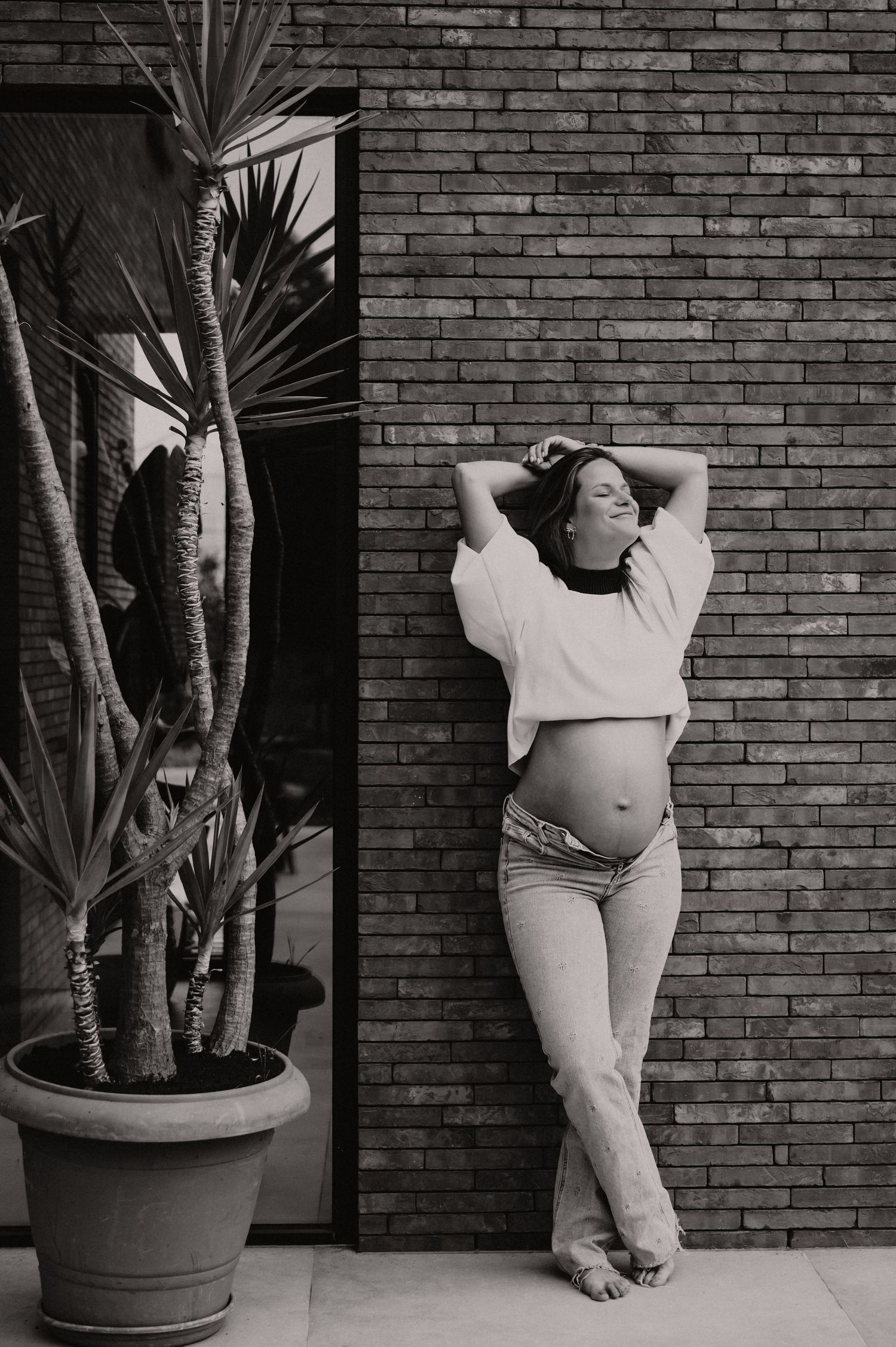 Zwangere vrouw poseert naast grote plant in zwart-wit, artistieke zwangerschapsfotografie West-Vlaanderen