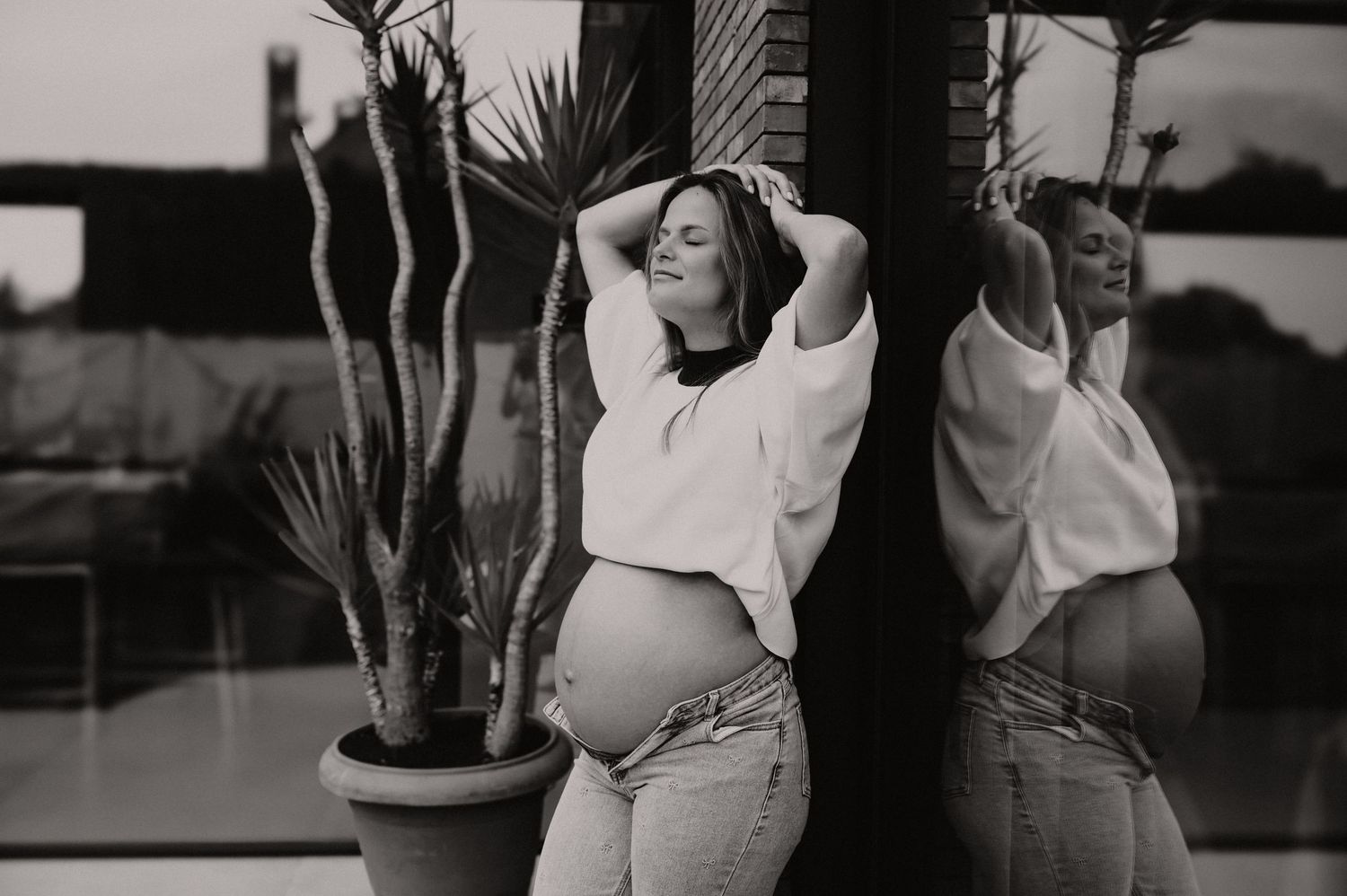 Zwangere vrouw poseert in zwart-wit in een gestileerde studio met plant, zwangerschapsfotograaf Roeselare