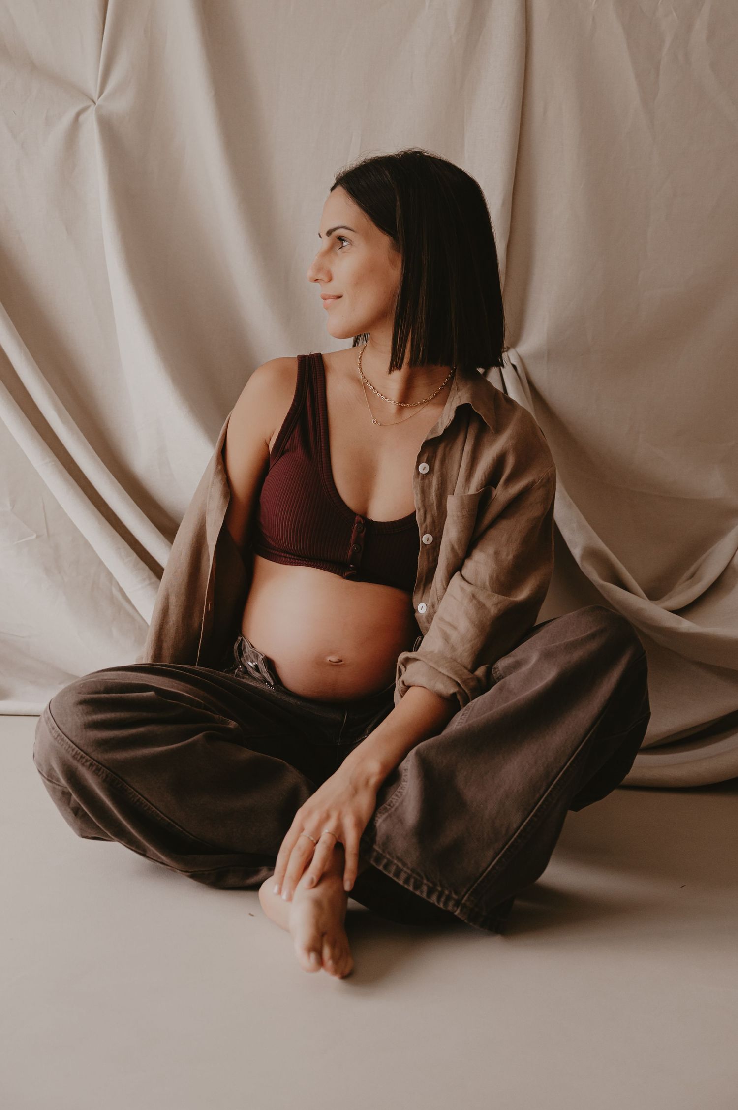 Zwangere vrouw zit gekruist met warme achtergrondverlichting, intieme lifestyle zwangerschapsfotografie Roeselare