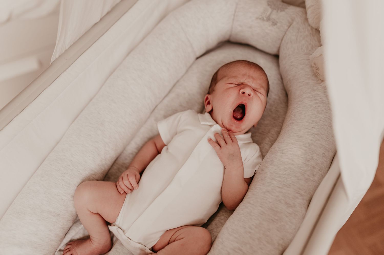 Pasgeboren baby Omer gaapt breed in zijn babynestje, newborn reportage aan huis Roeselare