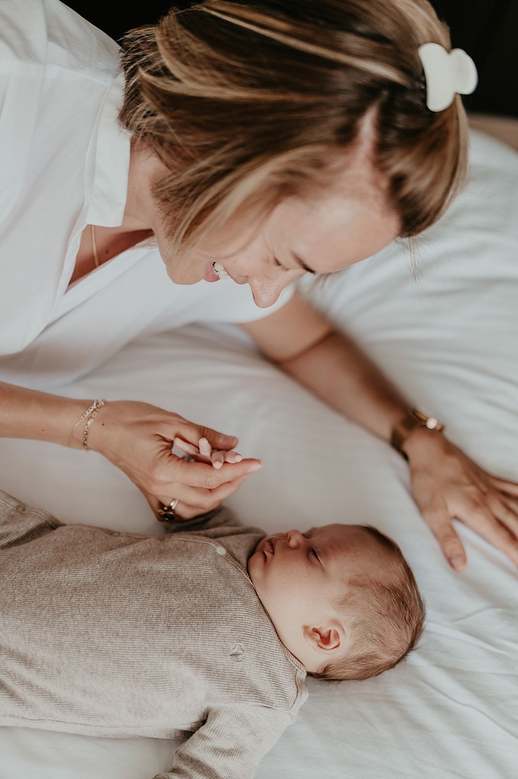 Mama leunt liefdevol over haar pasgeboren baby en houdt zijn handje vast, newborn shoot Roeselare