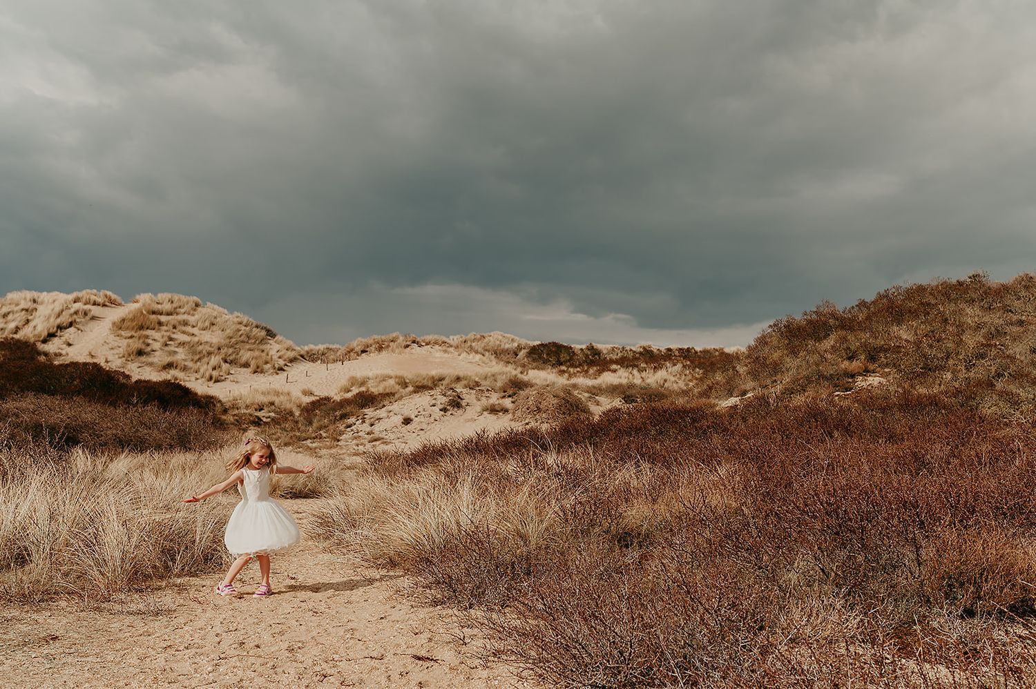 Meisje in witte jurk staat in de duinen tijdens communiefoto, feestneuzen fotograaf West-Vlaanderen