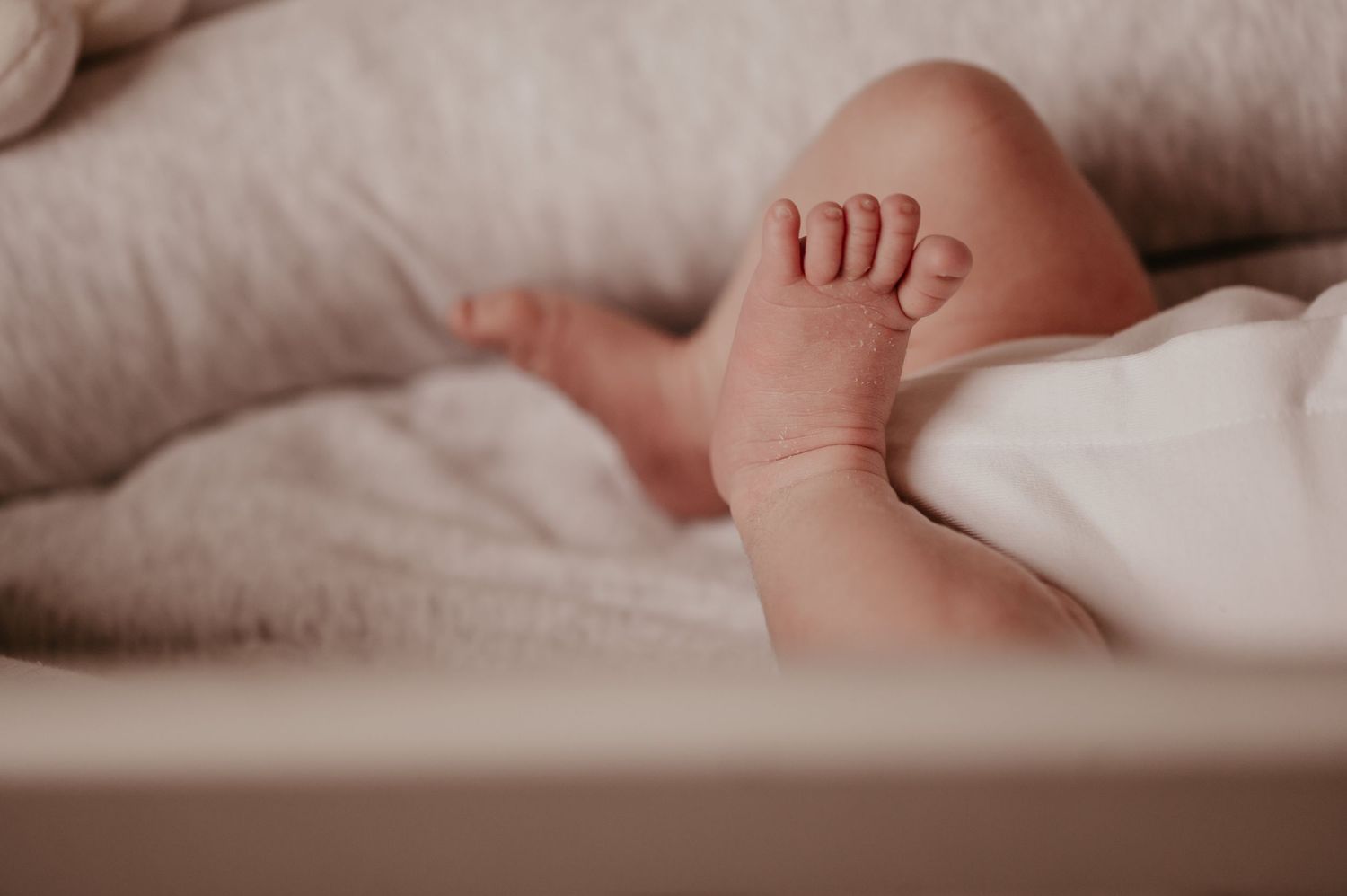 Detail van kleine babyveetjes in witte romper op zachte ondergrond, newborn reportage West-Vlaanderen