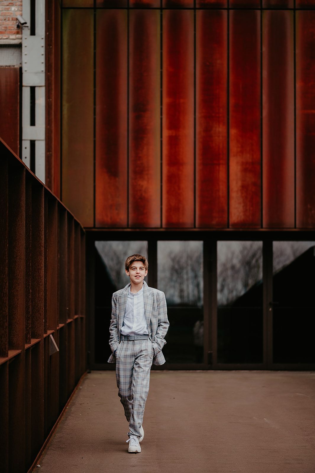Jongen in grijs pak poseert voor zijn communiefoto bij moderne architectuur, communiefotograaf West-Vlaanderen