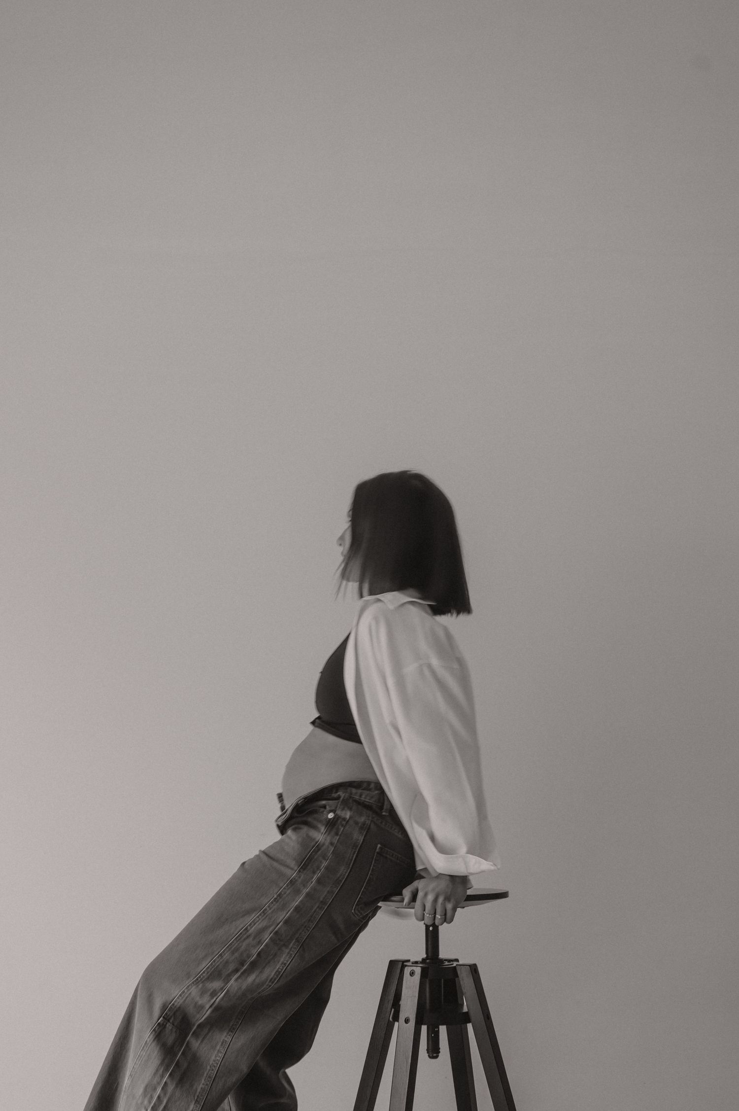 Zwangere vrouw staat sierlijk van achter in zwart-wit met ronde buik, elegante zwangerschapsfotografie Roeselare
