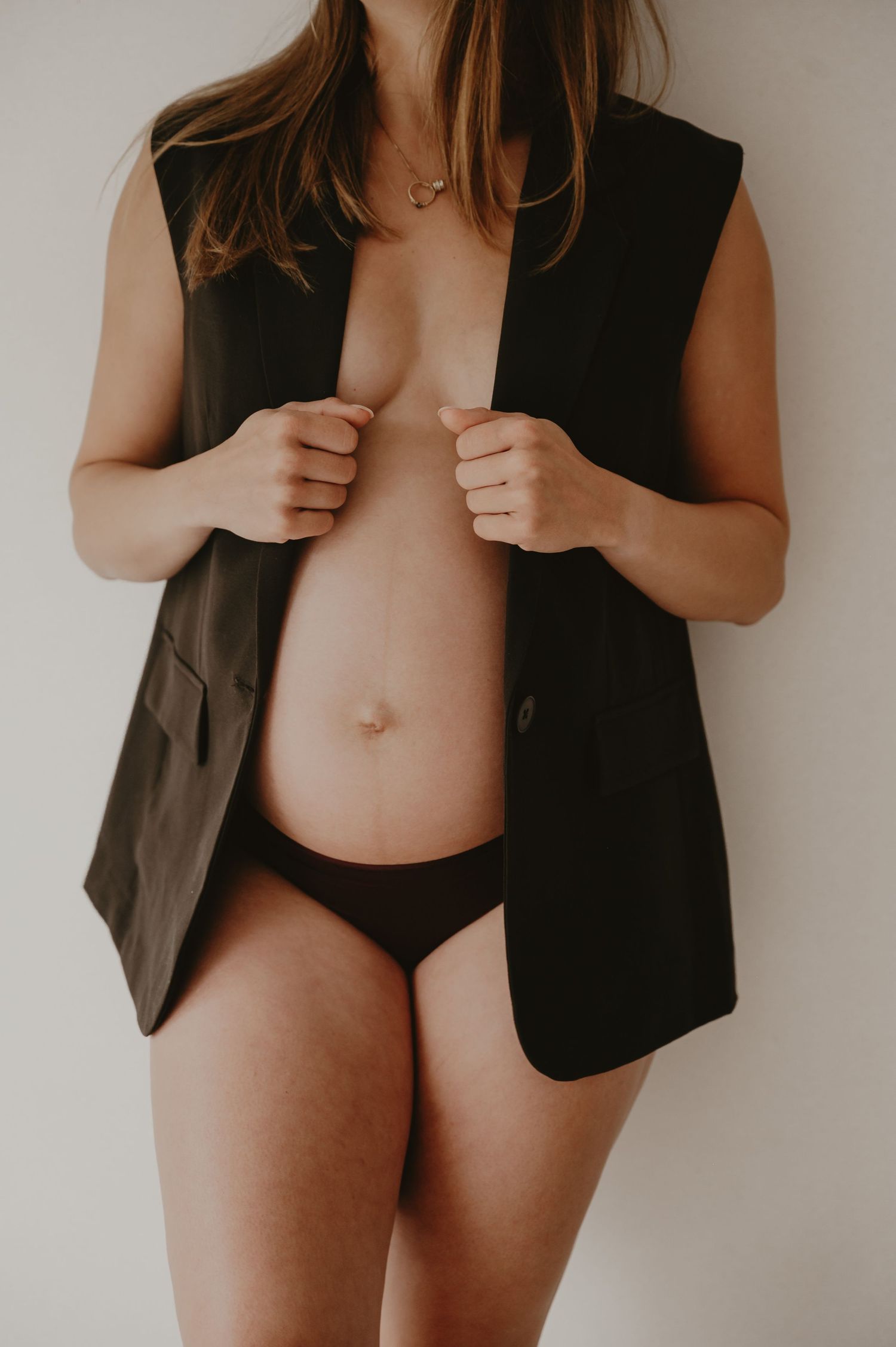Zwangere vrouw in zwart vest houdt liefdevol haar buik vast, zwangerschapsfotografie studio Roeselare