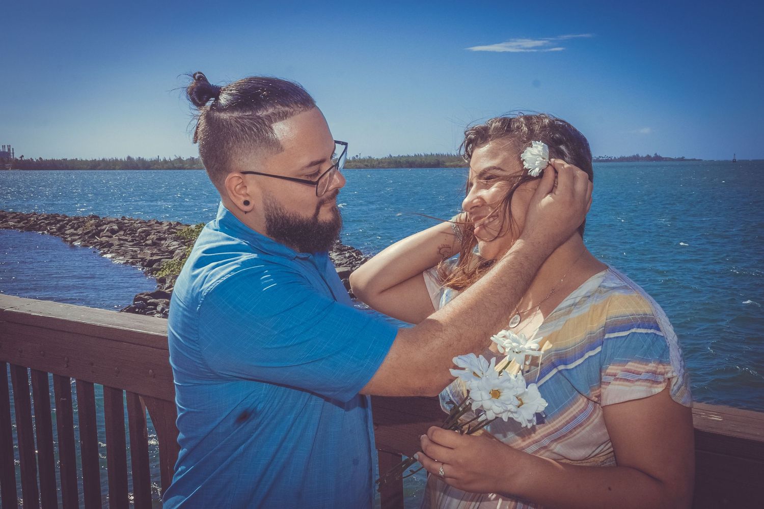 A tender moment between a couple on a seaside deck with blue waters in the background.