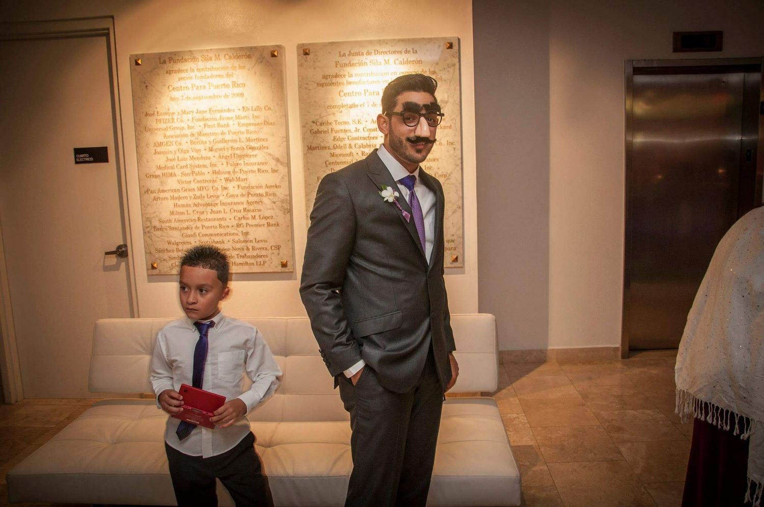 A formal event setting with suited attendees standing near decorative wall panels.