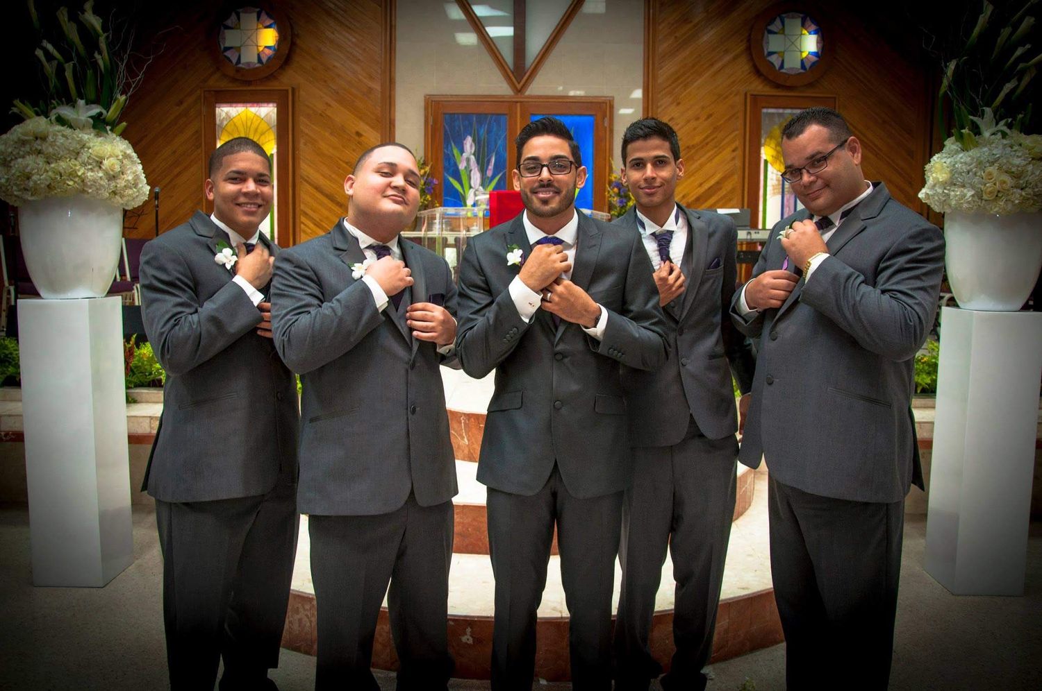 Groomsmen in matching gray suits pose playfully while making gestures at a wedding ceremony.