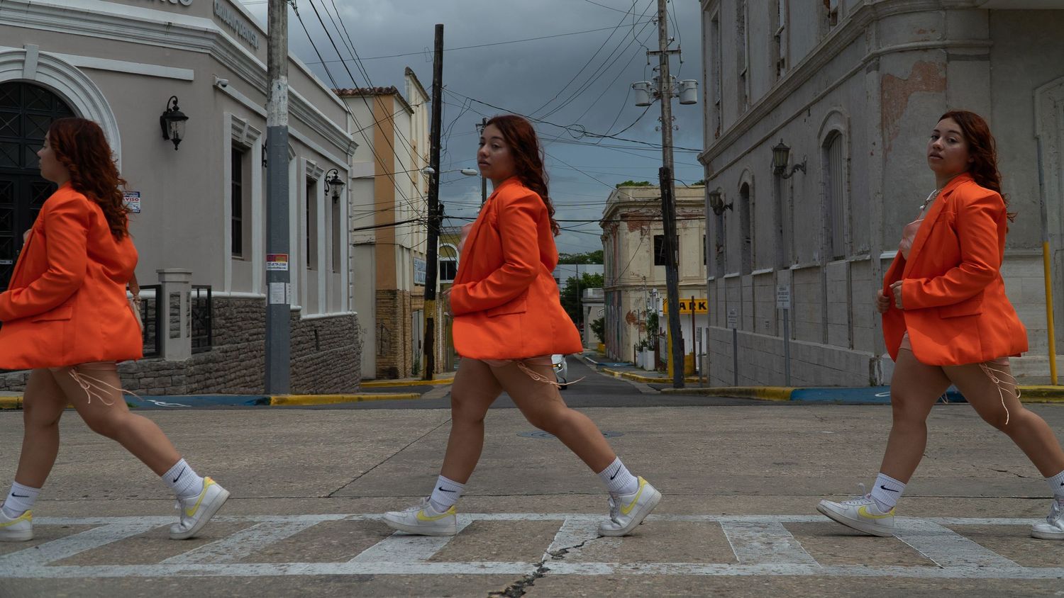 Three people in bright orange outfits perform synchronized walking across a crosswalk.