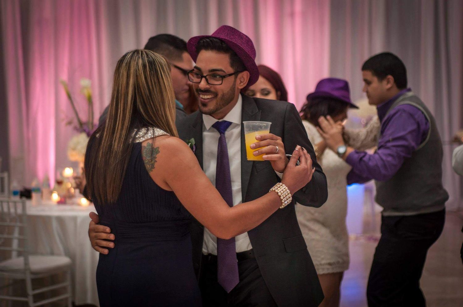 Couples dancing and enjoying themselves at an elegant wedding reception with pink lighting.