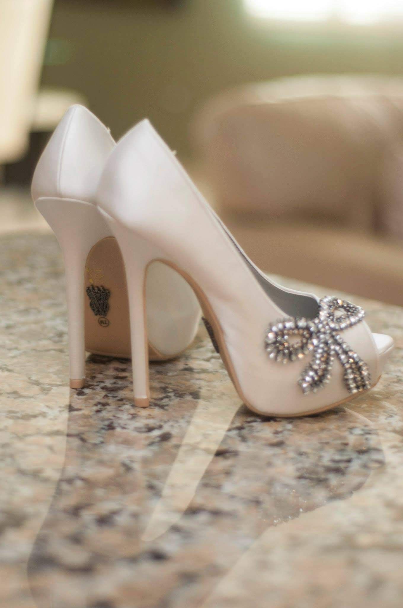 Elegant white bridal heel with crystal bow detail rests on granite countertop.