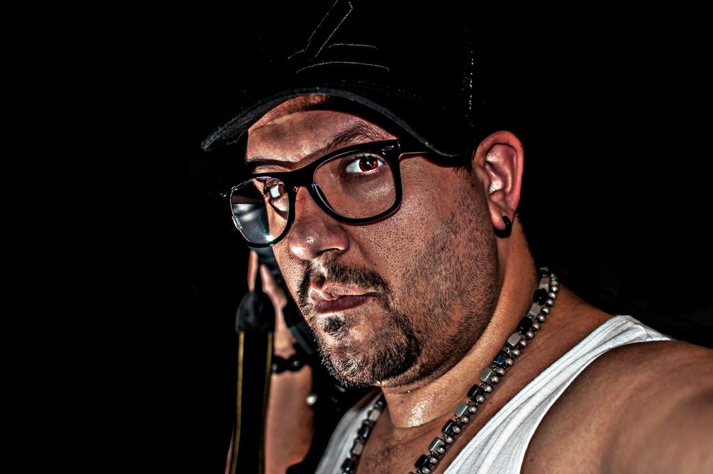 Dramatic side-lit portrait of person in baseball cap and glasses against black backdrop.