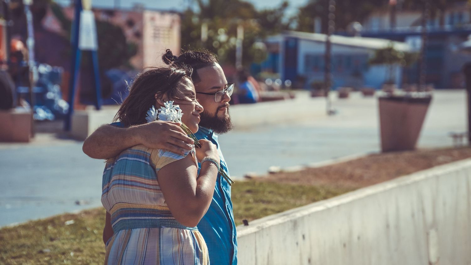 A couple shares an intimate embrace against an urban waterfront backdrop.