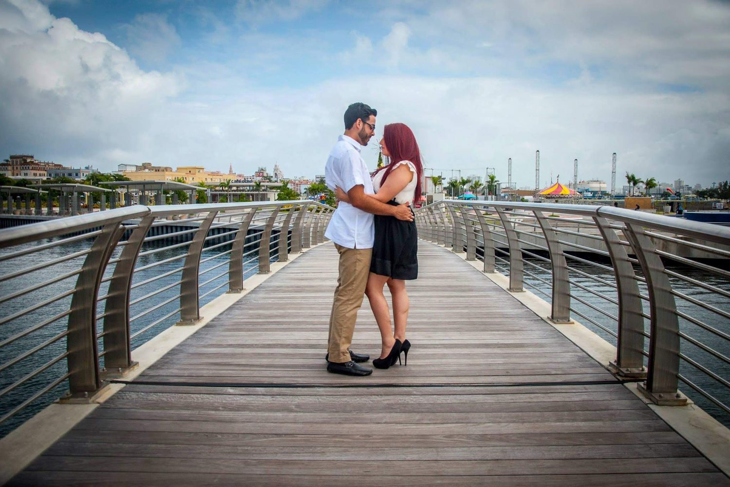 Romantic couple standing close together on wooden boardwalk with waterfront view.