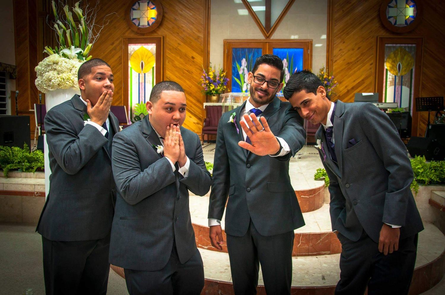 Groomsmen in dark suits make silly faces and gestures for a candid wedding photo.