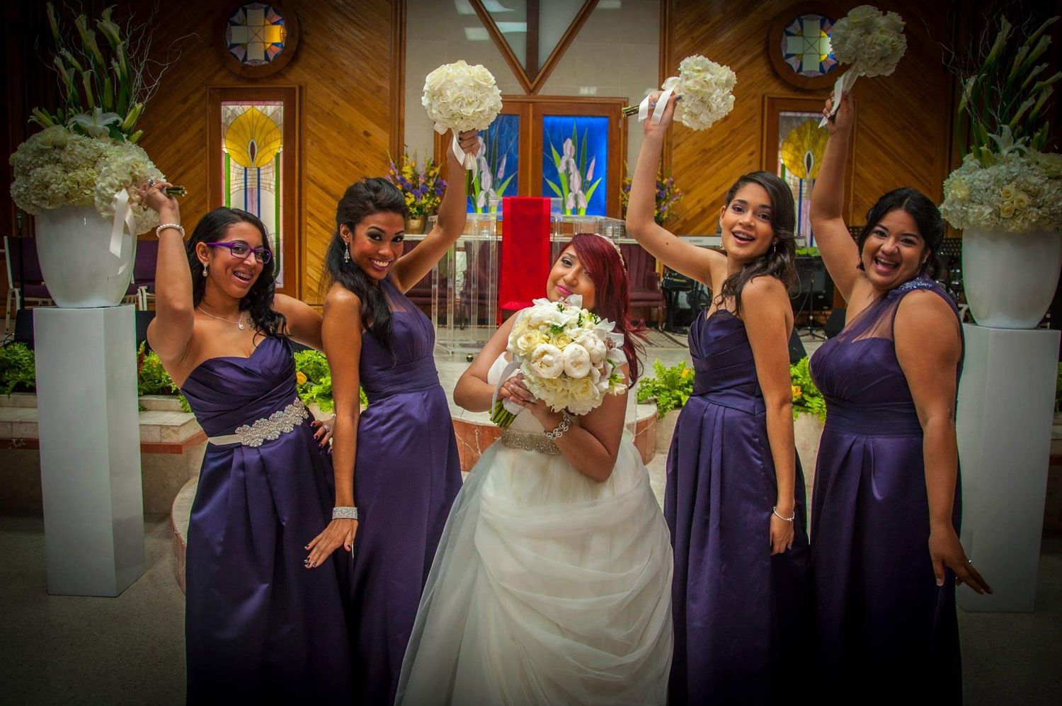 Wedding party with bridesmaids in purple dresses pose playfully for a fun group photo.