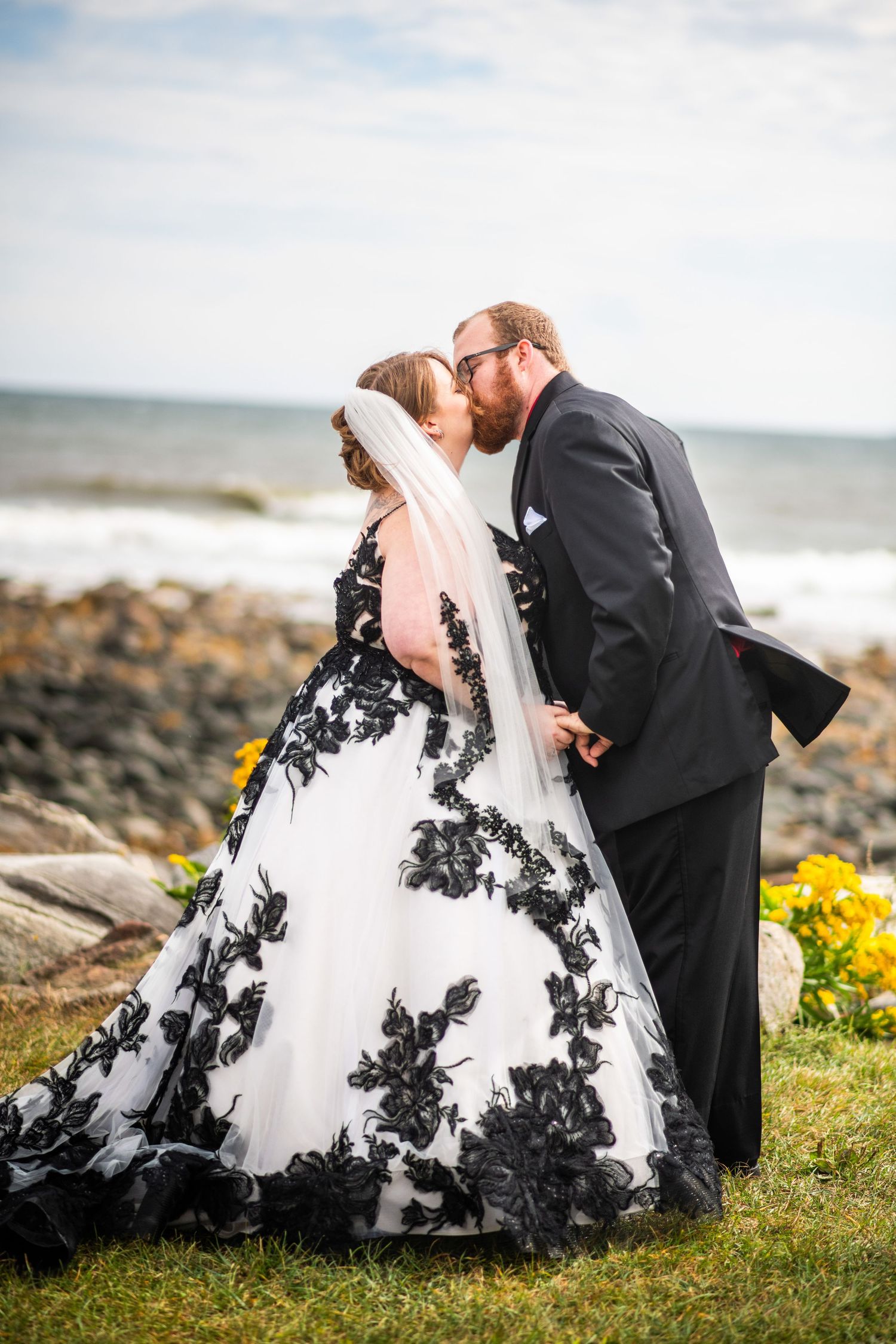 Newlyweds in dramatic pose by ocean with bride wearing black and white wedding gown.
