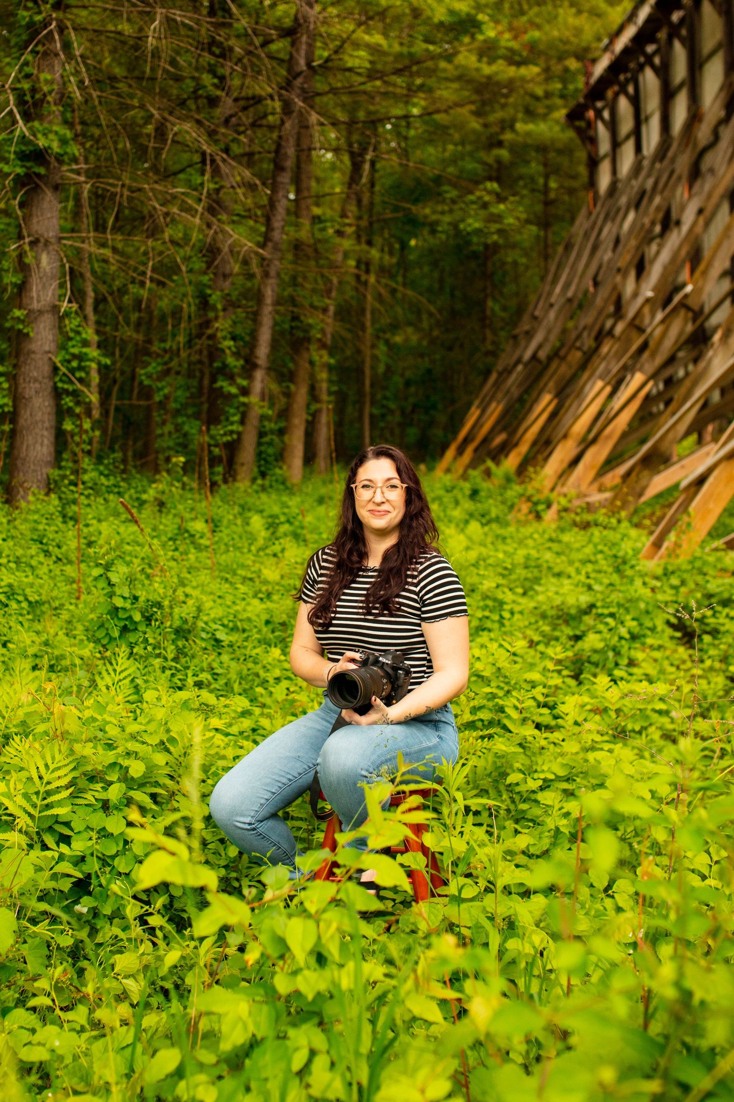 Person relaxing among lush green foliage in wooded area wearing casual striped shirt.