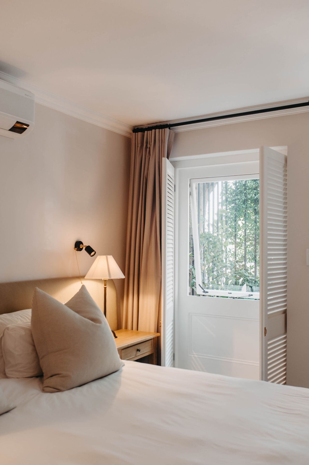 A series of minimalist bedroom interior shots showing white bedding, window shutters, and warm lighting in a cozy space.